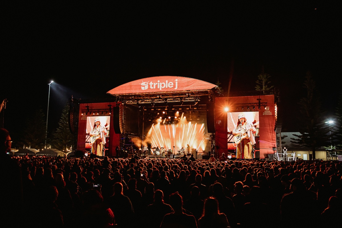 Musician Ruby Fields performing live on the illuminated triple j One Night Stand main stage at night in front of a massive outdoor crowd.